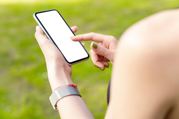 Young caucasian woman wearing sports bra standing on city park, outdoors hands holding phone with mockup white blank display, empty screen for social media. Mobile app tech concept.