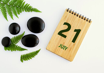July 21. 21th day of the month, calendar date. Notepad, black SPA stones, green leaves. Summer month, day of the year concep
