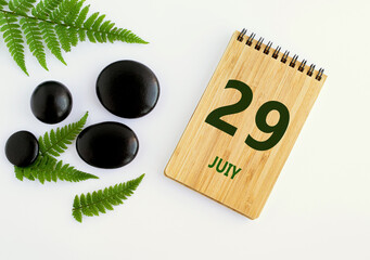 July 29. 29th day of the month, calendar date. Notepad, black SPA stones, green leaves. Summer month, day of the year concep