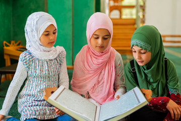 Wall Mural - A group of children reads the holy book Quran in the mosque. Happy Muslim family. Muslim girls in hijab learning about Islam religion.	