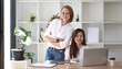 © wichayada - Two middle-aged women are looking at the camera while sitting on a desk in the office. female executives working in the office discussing documents