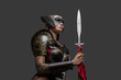 Studio shot of seductive woman barbarian dressed in armor and helmet holding spear.