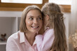 Cute little girl whispers to ear, share secrets with mom, parent looking interested and curious while listen her preschool daughter. Trust between mother and child, good trustworthy relations concept