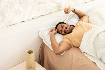 Wall Mural - Joyful Arabic Man Awakening Stretching Arms Lying In Bedroom Indoors