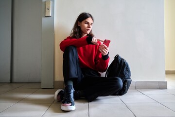 Teenage trendy male with smartphone backpack sitting on the floor