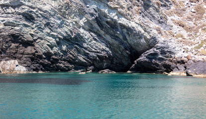 Wall Mural - Aegean Sea. Rocky coast, cliff and cave, Cyclades Greece, Rippled water near Nios island