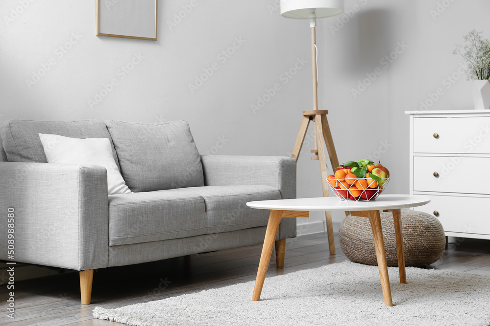 Table with fruit basket and sofa near light wall in living room