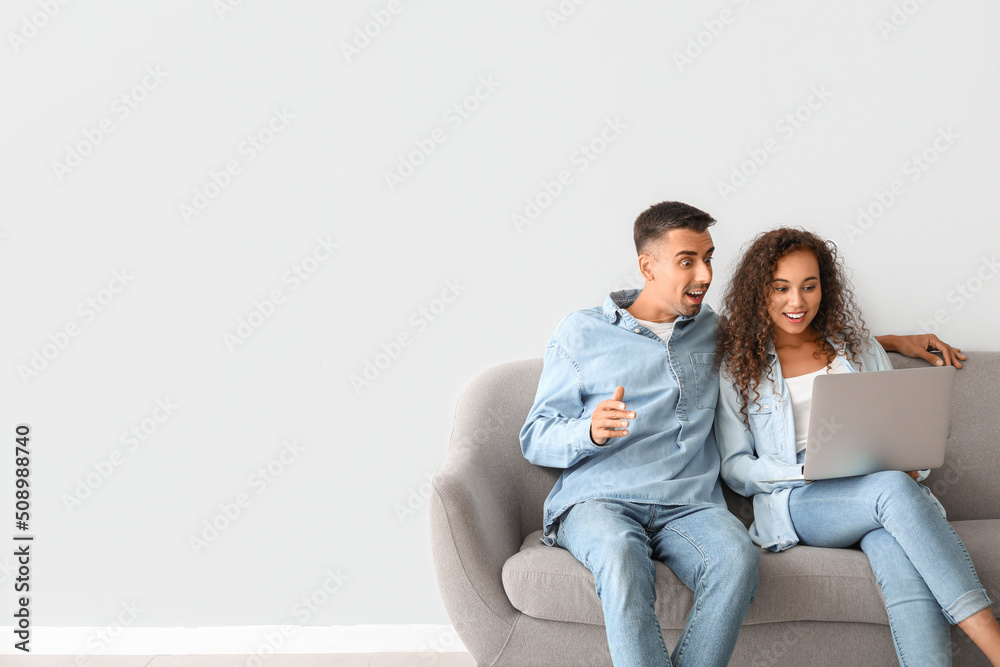 Surprised young couple using laptop on sofa near light wall