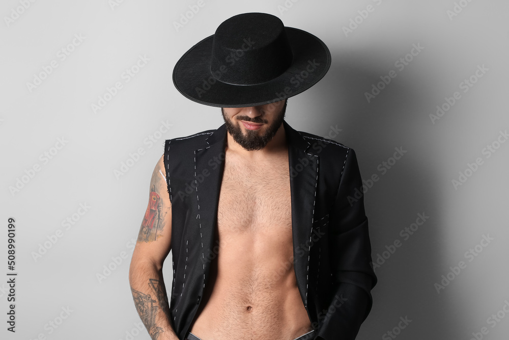Young bearded man in half-finished jacket and stylish hat on light background