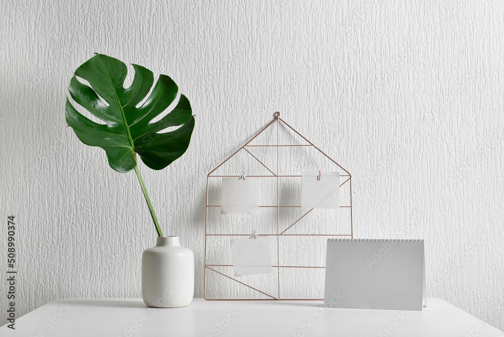 Workplace with palm leaf in vase, sticky notes and calendar near light wall