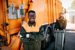 Caucasian and Black young garbage men working together on emptying dustbins for trash removal.