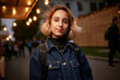 © Vladibulgakov - evening portrait of a beautiful young girl dressed in a denim jacket with a backpack. girl dressed in casual style. night portrait of a girl in a denim jacket