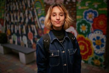 evening portrait of a beautiful young girl dressed in a denim jacket with a backpack. girl dressed in casual style. night portrait of a girl in a denim jacket