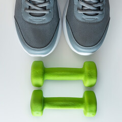 grey sneakers on a white background with two dumbbells for fitness