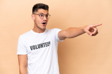 Young volunteer caucasian man isolated on beige background pointing away