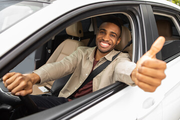 Wall Mural - Young african american man smiling while driving a car showing thumbs up recommending something good.