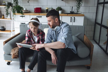 Handsome young strong father and his teenage son spending quality time together, having fun, enjoying togetherness. Boy playing tablet, learning, listen to music, dad helps