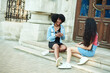 © etonastenka - An African American woman communicates with her friend. sitting on the stairs of the campus. Students are discussing classes at the university