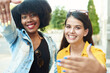 © etonastenka - Two beautiful girls of different nationalities show the photo frame with their hands and smile at the camera. Young girlfriends take a selfie on a city street