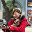 Latin woman using her smartphone and laughing while holding her dog