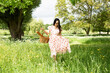 © Cavan Images - beautiful Asian woman walking in a field with picnic basket in summer
