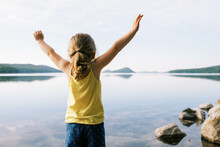 Little Toddler Girl Lifting Arms With Joy By A Serene Lake