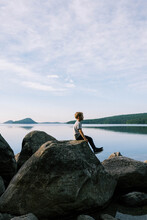 Boy Sitting On Big Boulder By A Crystal Clear Lake In New England