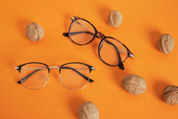 Wall Mural - trendy eye glasses on an orange background with walnuts, glasses for study and reading