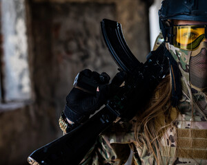 Portrait of a woman in a helmet and goggles with a machine gun in her hands. A female soldier in a camouflage uniform holds a weapon.