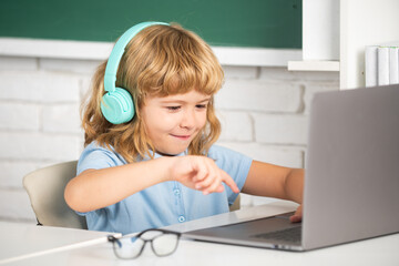 Smart boy in headphones sit at desk, study online on laptop at school, klever kid wear earphones in notebook learning using internet lessons. Online learning technology.