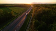AERIAL: Convoy Of Cargo Trucks On A Countryside Highway In Beautiful Golden Light. Low Traffic On A Motorway That Crosses Beautiful Landscape In Gorgeous Light. Truck Transport For Delivering Goods.