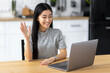 © kucherav - Happy Asian woman freelancer, young female student using a laptop sitting in home, having video call, learning language. Freelancer working remotely, discussion something
