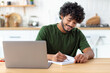 © kucherav - Portrait of confident asian young man. Successful student or freelancer sitting at workplace and working using laptop, smiling friendly. Distant work, e-learning concept
