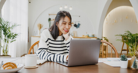 Wall Mural - Young asia lady freelance focus on presentation work in laptop for account and finance project for remote meeting with company in kitchen at house. Girl student learn online at home.