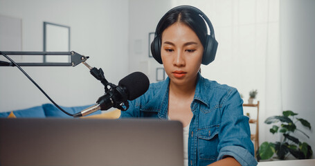 Wall Mural - Happy asia girl record a podcast on laptop computer with headphones and microphone talk with audience at living room. Female podcaster make audio podcast from her home studio. Stay at house concept.