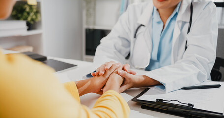 Close up of young Asia female doctor in white medical uniform talk discuss touching girl patient shoulder at meeting sitting at desk in health clinic or hospital office. Psychological help concept.