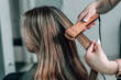 © Вера Щербакова - Woman hairdresser straightens brown hair of a beautiful woman using hair tongs in a beauty salon. Female stylist makes a hairstyle for a young beautiful woman in a barbershop.