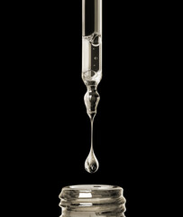 Oily drop dripping from pipette into cosmetic bottle close up on a black background
