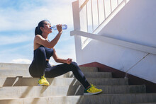 Tired Runner Woman With A Bottle Of Electrolyte Drink Freshness After Training Outdoor Workout At The Stadium Stairway.