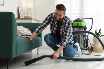 Poster - Man vacuuming floor under sofa in living room