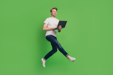 Profile photo of crazy energetic man hold laptop jump enjoy distance work wear white t-shirt on green color background