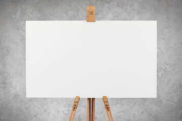 a blank artist's canvas on an easel against a concrete wall background.