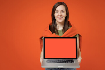 Wall Mural - Young smiling happy woman 20s in khaki t-shirt tied sweater on shoulders hold use work on laptop pc computer with blank screen workspace area look camera isolated on plain orange background studio