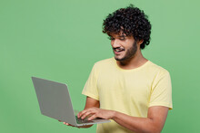 Young Smiling Happy Indian Man 20s In Basic Yellow T-shirt Hold Use Work On Laptop Pc Computer Chatting Online Isolated On Plain Pastel Light Green Background Studio Portrait People Lifestyle Concept