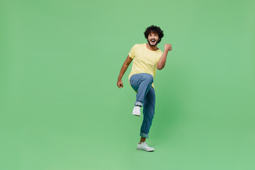 Wall Mural - Full body young smiling Indian man 20s in basic yellow t-shirt doing winner gesture celebrate clenching fists say yes isolated on plain pastel light green background studio. People lifestyle concept.