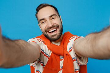 Poster - Close up young smiling cheerful happy man 20s in orange striped t-shirt look camera doing selfie shot pov on mobile phone isolated on plain blue background studio portrait. People lifestyle concept