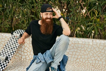 Canvas Print - Young irish skater man smiling happy sitting on the bench at the park.