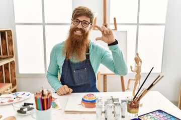 Canvas Print - Redhead man with long beard painting clay bowl at art studio smiling and confident gesturing with hand doing small size sign with fingers looking and the camera. measure concept.