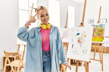 Canvas Print - Young caucasian girl at art studio smiling pointing to head with one finger, great idea or thought, good memory