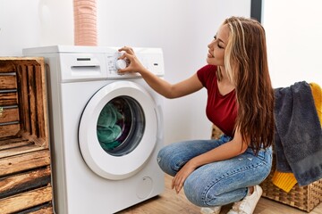 Poster - Young caucasian girl smiling happy cleaning clothes using whasing machine at home.